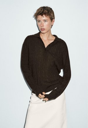 Brown knitted sweater with a cable pattern, featuring a collared neckline and long sleeves, paired with a white skirt.