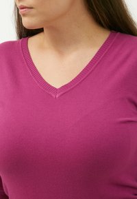 Taillierter V-Ausschnitt-Pullover in lebhaftem Magenta. Weicher Strick mit geripptem Halsauschnitt und nahtlos integrierten Schulterdetails.