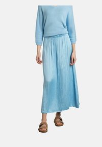 Jupe maxi plissée bleu clair avec taille élastique, associée à un pull bleu assorti et des sandales brunes. Texture douce et fluide.