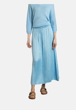 Jupe maxi plissée bleu clair avec taille élastique, associée à un pull bleu assorti et des sandales brunes. Texture douce et fluide.