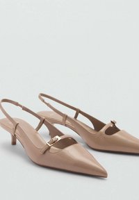 Tacones slingback en beige con punta afilada, que presentan un pequeño tacón kitten, un diseño con recortes y un detalle de hebilla dorada en la correa. Textura de cuero suave.