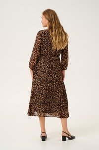 Maxi-mekko, jossa on leopardikuosiset läpikuultavat kankaat, kolmannelta osalta hihat ja elastinen vyötärö. Mustat paksupohjaiset kengät viimeistelevät asun.