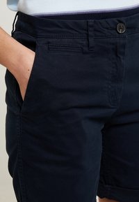 Granatowe szorty wykonane z tkaniny z mieszanki bawełny, z zapięciem na guzik, bocznymi kieszeniami oraz płaskim przodem o gładkiej fakturze.