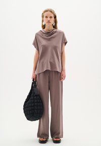 Blusa corta e ampia a maniche corte di colore malva con scollo a gore, abbinata a pantaloni coordinati. Tiene una borsa a tracolla nera e trapuntata in stile hobo. Sandali flat.
