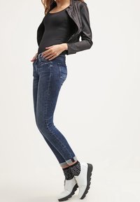 Jeans ajustados de mezclilla azul oscuro, combinados con una camiseta negra ajustada y una chaqueta de cuero negra. Botines blancos con una suela gruesa y calcetines con estampado.