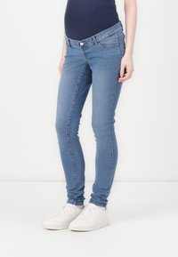 Skinny light blue jeans made of denim with a mid-rise waist, featuring a button closure and subtle pocket stitching. Paired with white shoes.