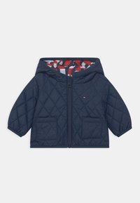 Tmavě modrá prošívaná bunda s kapucí, opatřená zipem, dvěma předními kapsami a kontrastní podšívkou s červenobílým vzorem.