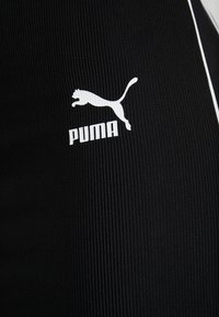 Tissu athlétique noir avec une texture côtelée, présentant un logo Puma blanc avec un design de chat sautant. Comprend de fines bandes blanches en accent.