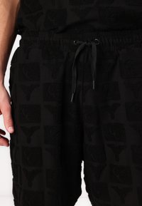 Black shorts made of textured fabric featuring an all-over pattern of square shapes with a raised design. Includes a drawstring at the waist.
