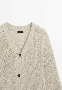 Beige gebreide cardigan met V-hals, lange mouwen en twee zwarte knopen aan de voorkant. Lichtgewicht, gestructureerde stof met een open geweven look.