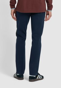 Pantaloni navy a gamba dritta, abbinati a sneaker nere e bianche con tre strisce, con una texture liscia e una finitura su misura.
