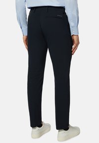 Pantalons marine à coupe slim. Confectionnés dans un matériau lisse, avec des poches arrière et un accent logo subtil. Portés avec des chaussures blanches.