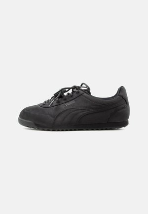 Czarny zamszowy sneaker Puma z czarnymi sznurowadłami i teksturowaną podeszwą, widziany od zewnętrznej strony na tle jednolitego jasnego tła.