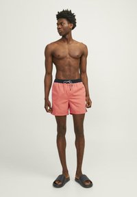 Roze zwembaden met een elastische tailleband en een zwarte trekkoord, gedragen met zwarte slippers, gepresenteerd op een staande model.