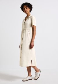 Abito midi in lino color crema con maniche corte, chiusura a bottoni e leggere pieghe in vita. Abbinato a sneaker bianche e beige.
