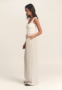 Let, cremefarvet tanktop kombineret med højttaljede, vidde-ben beige bukser; blødt stof, rene linjer og sidelommer.