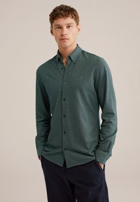 Zelena srajca z dolgimi rokavi in gumbi, izdelana iz tkanine z teksturo, s klasičnim ovratnikom, gumbi spredaj in majhnim vezenim poudarkom.