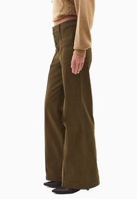 Olive zielone spodnie o szerokich nogawkach, wykonane z mocnego materiału, z wysokim stanem w talii i czarnymi guzikami oraz starannie wykończonym dołem.
