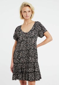 Schwarzes Blumenkleid mit kurzen Ärmeln, V-Ausschnitt, Knopfdetails und gestuftem Rüschensaum, das hellrosa und weiße Blättermuster auf dem Stoff zeigt.