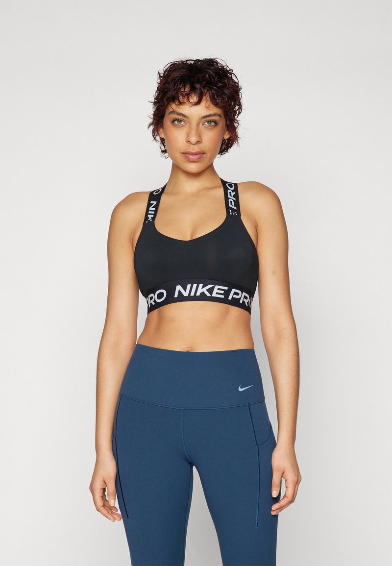 Crna sportska brusnica sa širokim trakama koja nosi "NIKE PRO" oznaku, uparen sa visokim tamnoplave tajice s bočnim džepovima i malim logotipom.