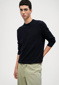 Ναυτικό πλεκτό πουκάμισο με μακριά μανίκια και ριμπ κολοσσό, συνδυασμένο με ανοιχτόχρωμο, φαρδύ παντελόνι.