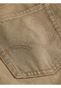 Nærbillede af en brun denimlomme med buet dobbeltsyning i matchende tråd på et par bukser eller jeans.