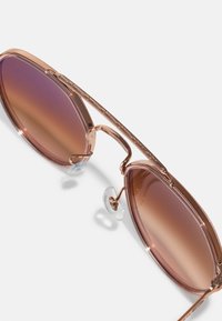 Ochelari de soare cu rame roz, cu lentile maronii cu gradient, având o formă elegantă și alungită și accente decorative pe rama metalică.