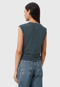 Grå ærmeløs t-shirt med rund hals, letvægtsstof, og et lille logo-detail på ryggen. Parret med højtaljede blå jeans.
