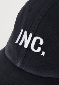 Fekete pamut sapka, az elején fehér hímzett "INC." felirattal. Strukturált kialakítás, ívelt napellenzővel és texturált anyaggal.