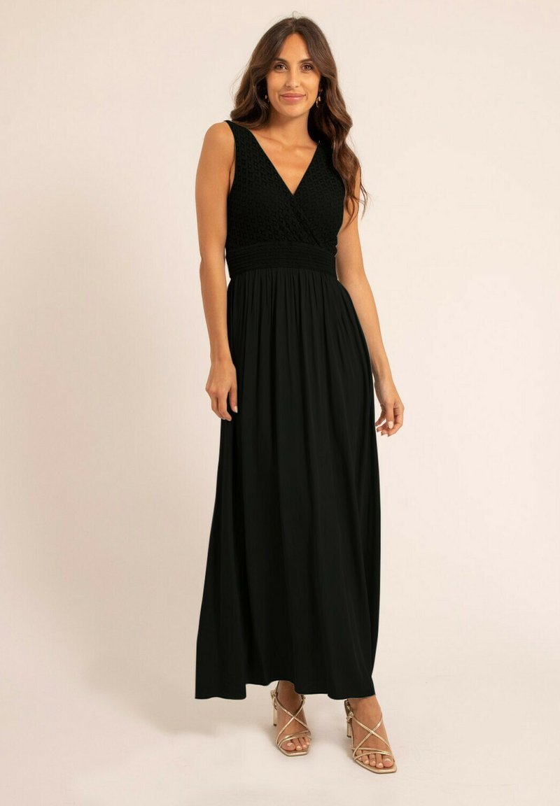 Robe maxi noire avec un corsage texturé et ajusté et une jupe fluide. Présente un décolleté en V profond et des bretelles larges, accompagnée de sandales à lanières.