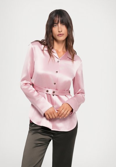 Camicia in satin rosa chiaro con maniche lunghe, chiusura a bottoni e vita sfiancata. Presenta un colletto a punta e una texture liscia.