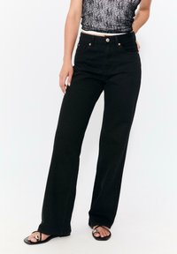 Svarta högmidjade jeans med rak bendesign. Har kopparfärgade knappar och sömnadsdetaljer. Materialet verkar vara denim.