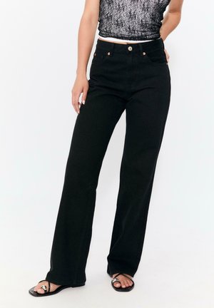 Jean noir taille haute avec une coupe droite. Présente des boutons et des coutures en ton cuivré. Le matériau semble être du denim.