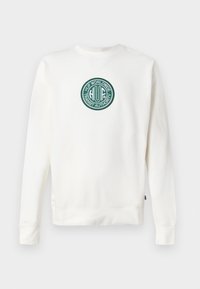Felpa crema con maniche lunghe, scollo rotondo e un logo circolare ricamato in verde che presenta la dicitura "HUF Worldwide Transit Authority."