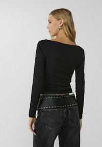 Black long-sleeve top with a boat neck, paired with high-waisted dark denim jeans and a wide black leather belt featuring silver studs.