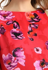 Tessuto rosso con un motivo floreale che presenta fiori viola e rosa. Il design è audace e vivace, con una texture liscia.