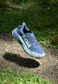 Scarpa da corsa leggera grigia e menta con tomaia testurizzata, logo prominente e suola robusta, progettata per durabilità e supporto su sentieri.