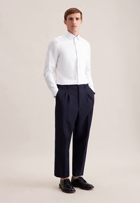 Weißes Hemd mit langen Ärmeln und Knöpfen, kombiniert mit dunkelblauen, plissierten Hosen und schwarzen Lederschuhen. Glatter Stoff, maßgeschneiderte Passform, klassisches Design.