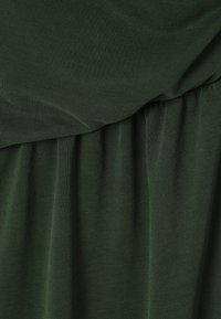 Dunkelgrüner Stoff mit geraffter und gefalteter Textur, der ein feines gewebtes Muster und einen weichen Fall zeigt.