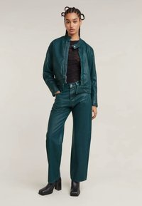 Teal Lederjacke mit Stehkragen, kombiniert mit tealfarbenen Leder-Breite-Hosen. Beide Teile haben eine glatte Textur und ein minimalistisches Design.