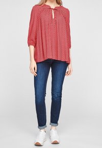 Blouse à motif rouge avec des manches trois-quarts et un décolleté en goutte d'eau, associée à un jean skinny bleu foncé et des baskets blanches.