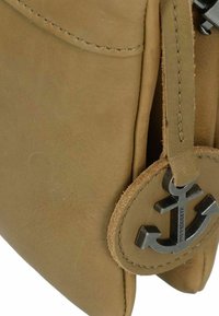 Borsa a tracolla in pelle marrone con texture liscia, dotata di un logo ancorato rotondo come accentuazione e cuciture visibili lungo i bordi.