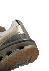 Zapatilla deportiva de color beige claro con un acento dorado, con un tacón texturizado y suela de goma que presenta un patrón de banda de rodadura multidireccional.