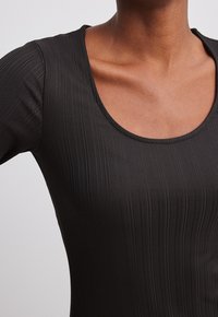 Body noir côtelé à manches longues avec un large décolleté en forme de scoop. Le tissu est lisse et moulant, mettant en valeur un motif texturé.