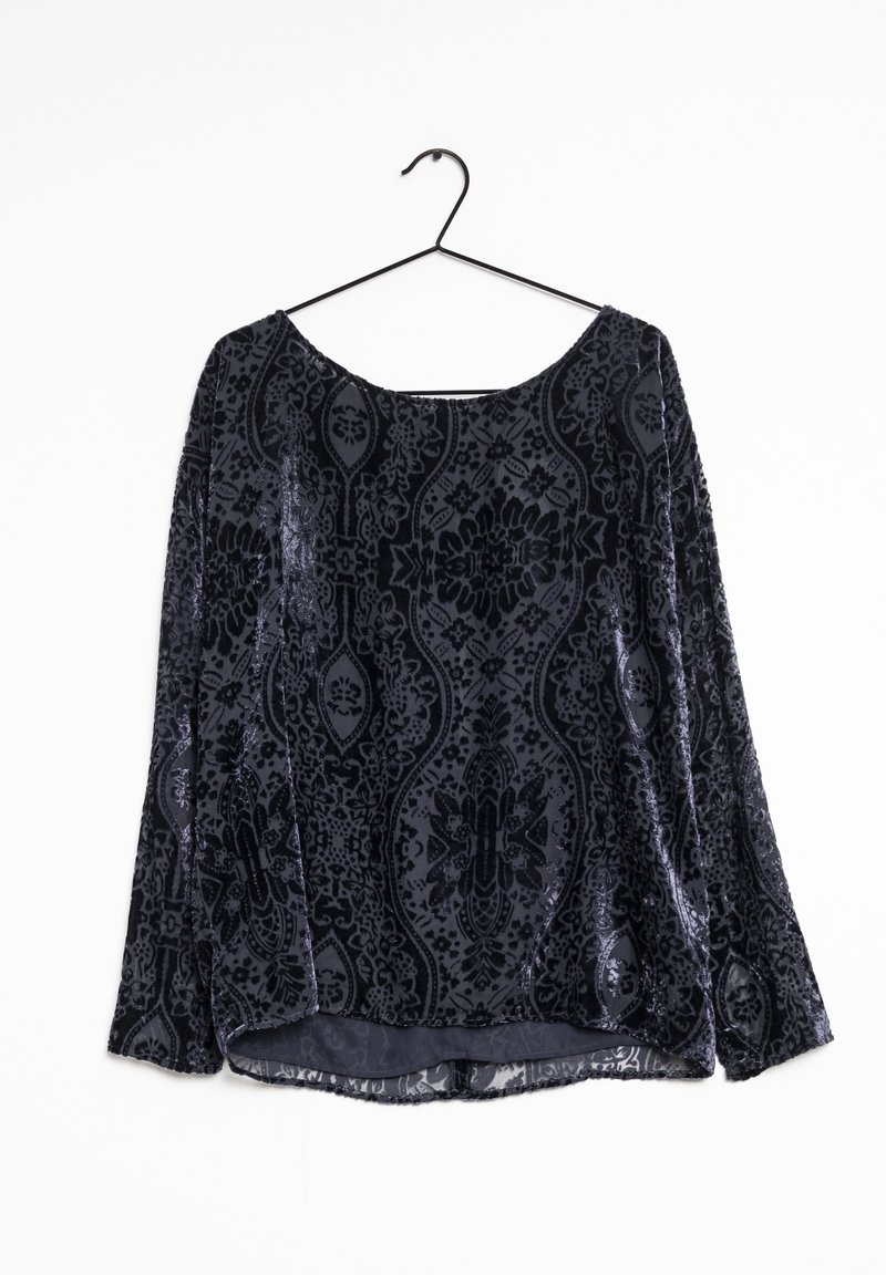 Haut en velours noir au design fluide, avec un motif orné, des manches longues et un col rond. Suspendu à un crochet noir.