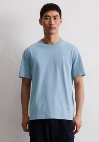 Light blue cotton t-shirt with a crew neckline. Features short sleeves and a small white logo on the left chest. Simple design, regular fit.