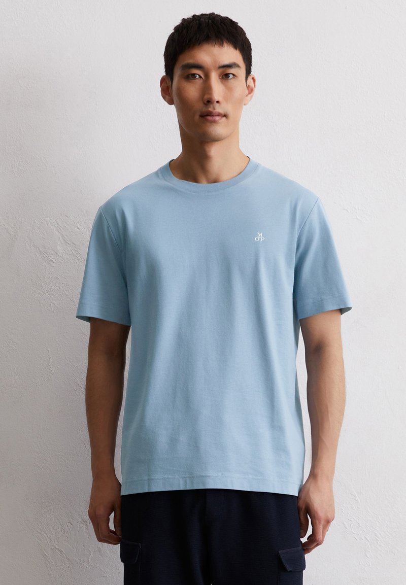 Light blue cotton t-shirt with a crew neckline. Features short sleeves and a small white logo on the left chest. Simple design, regular fit.