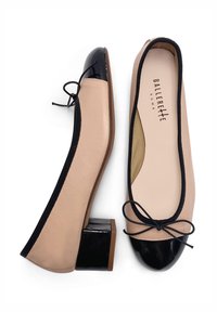 Ballerine in pelle nuda con punta in vernice nera, dotate di un piccolo tacco a blocco e un dettaglio in nastro nero a fiocco lungo l'apertura.
