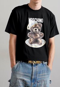 Must svart puuvillane t-särk, millel on prinditud pilt pruunist karust, kellel on seljas hõbedane kaas, brändiga "Moschino" julgete valgete tähtedega.