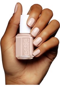 Bottiglia di smalto per unghie con base quadrata in vetro, tappo bianco e smalto rosa chiaro. Mano che mostra unghie rosa chiaro perfettamente curate.